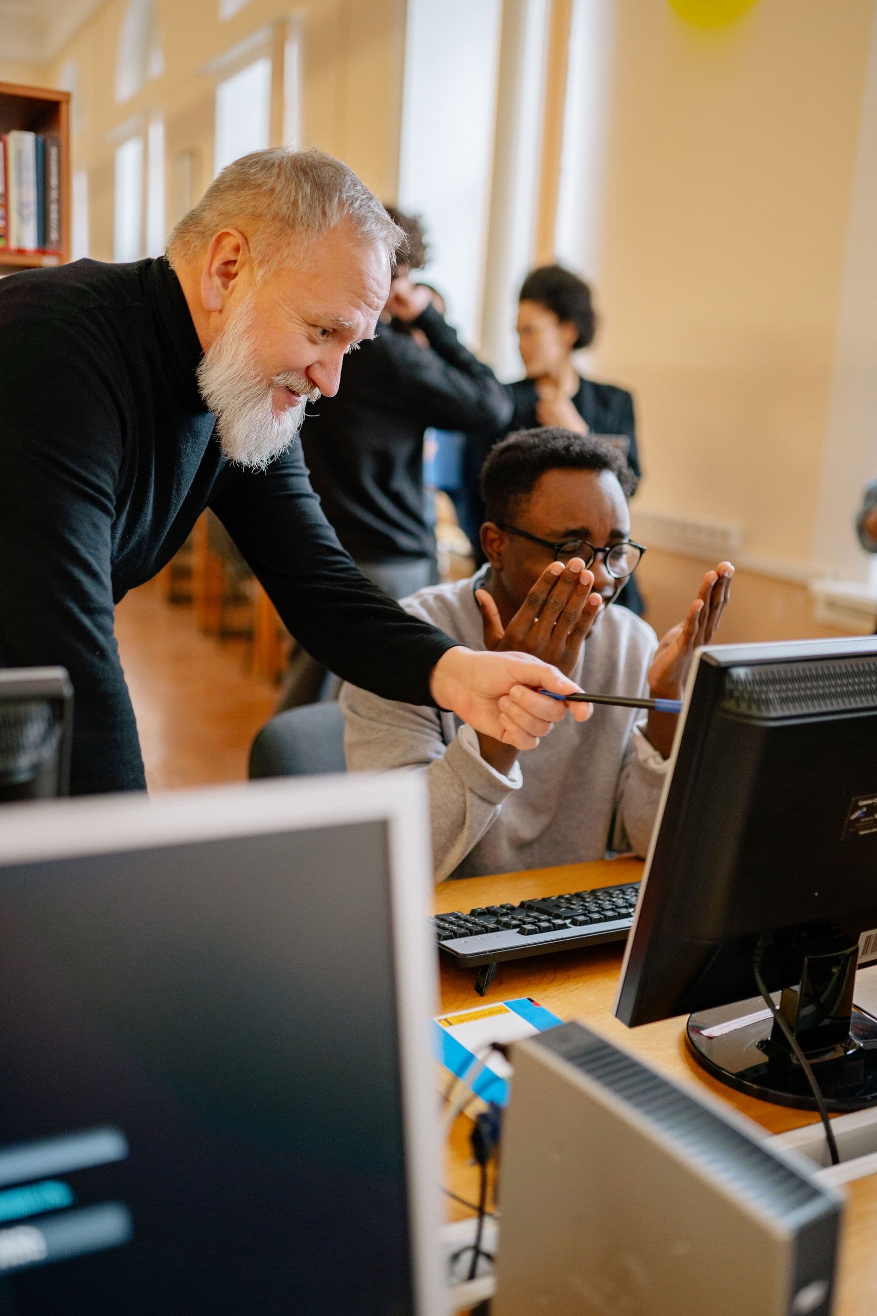 A mentor pointing something out on screen while a delighted student looks on