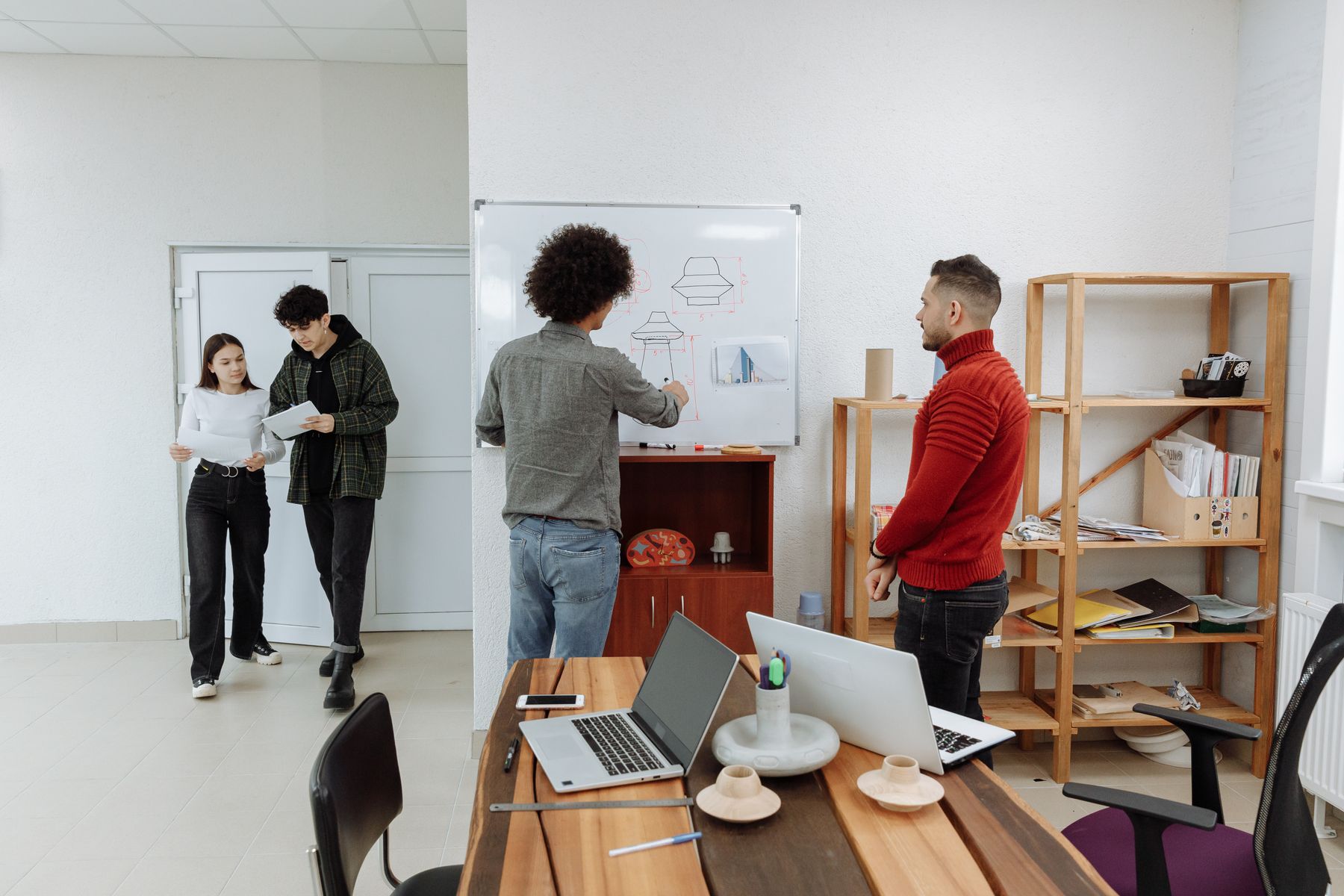 A small startup team gathered at an office whiteboard, talking through a product sketch